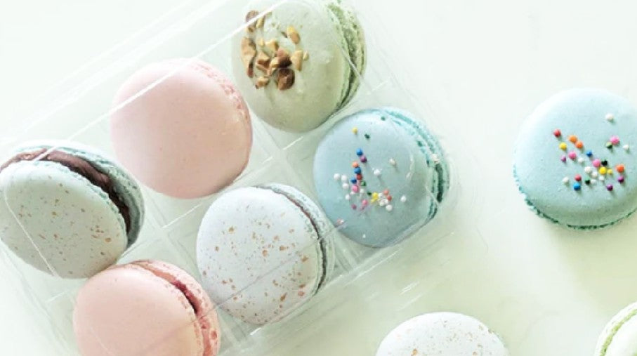 Beautifully decorated macarons in a clear container.
