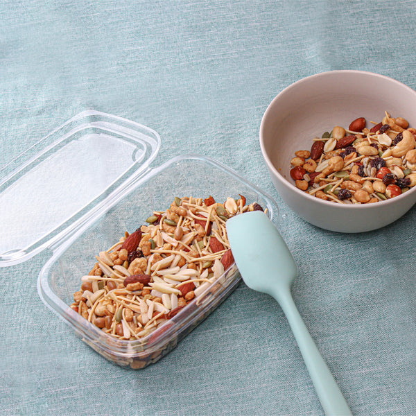 Trail mix in  a clear container being added to a bowl for guests.