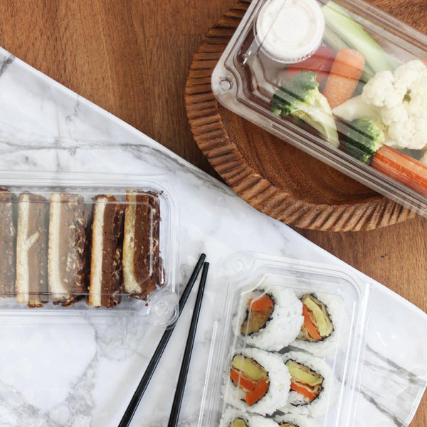 Center sealed biodegradable 16 oz food containers made of clear, compostable plastic containing fresh vegetables, sushi, and baked goods