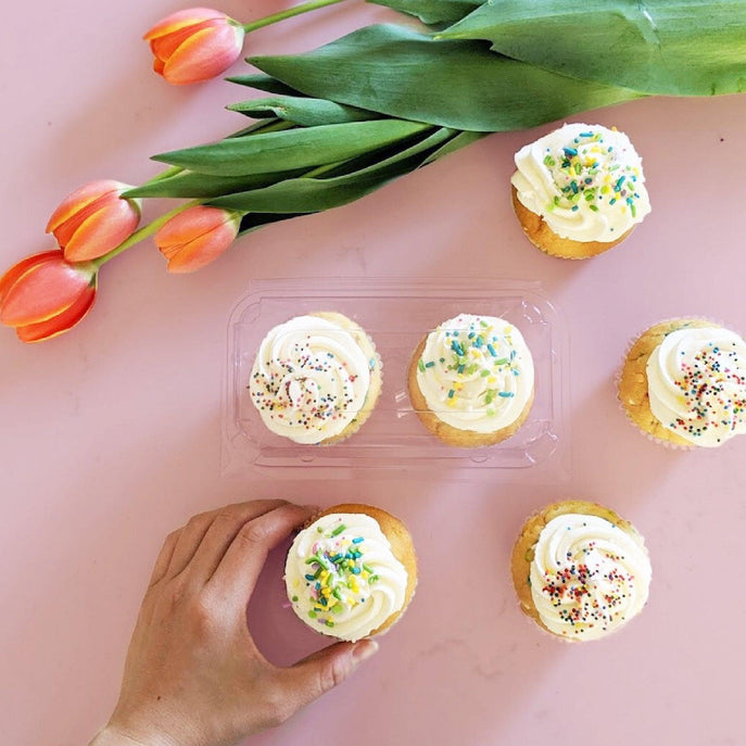 2-pack 3" Cupcake & Muffin Packages made of clear, compostable plastic beside an assortment of tulips and cupcakes
